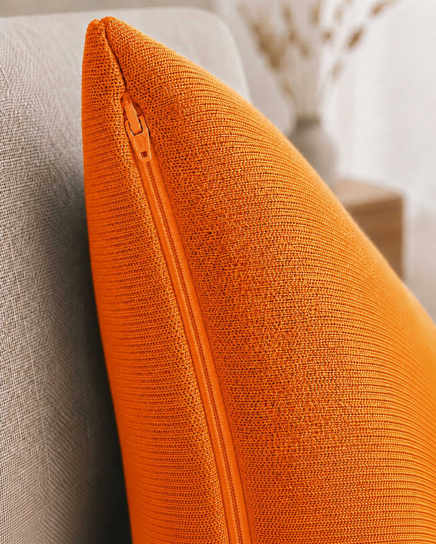 Detailaufnahme eines orangenen Dekokissens mit sichtbarem Reißverschluss auf einem beigen Sessel.