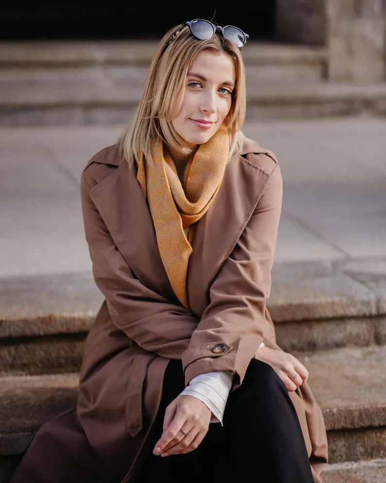 Outfit mit Strickschal in Curry-Melange getragen von Frau in braunem Mantel im herbstlichen Look.
