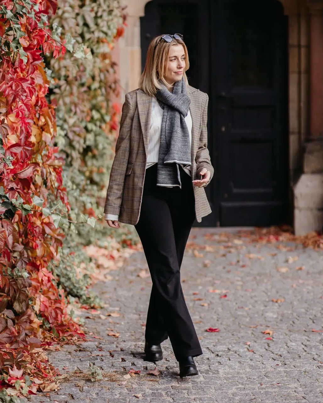 Frau trägt Strickschal in Grau-Melange vor herbstlicher Kulisse im Lifestyle-Bild.