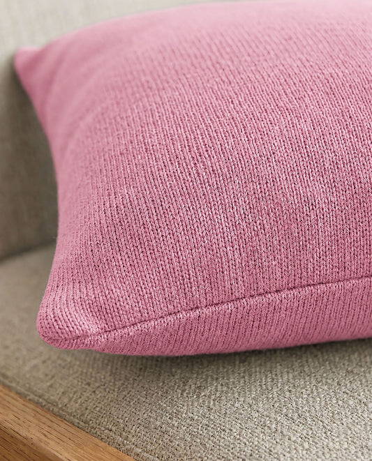 Nahaufnahme eines rosa Dekokissens, das auf einem beigefarbenen Polstermöbel mit Holzrahmen liegt