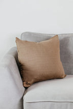 Beiges Strick-Dekokissen auf einem hellgrauen Sofa vor einer weißen Wand.