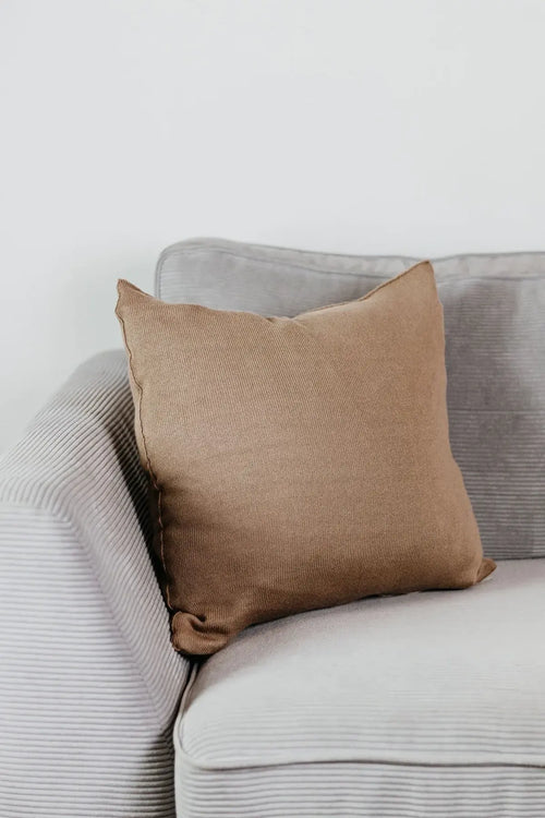 Beiges Strick-Dekokissen auf einem hellgrauen Sofa vor einer weißen Wand.