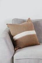 Beiges Strick-Dekokissen mit cremefarbenem Streifen auf einem hellgrauen Sofa vor einer weißen Wand.