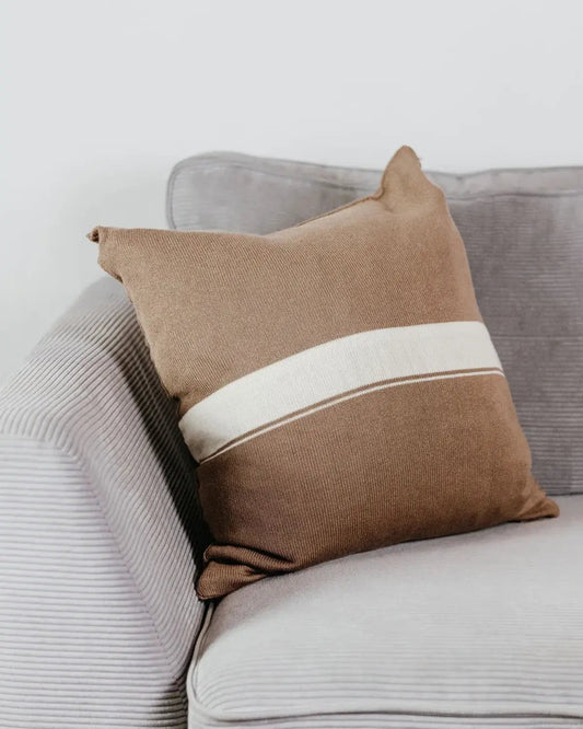Beiges Strick-Dekokissen mit cremefarbenem Streifen auf einem hellgrauen Sofa vor einer weißen Wand.