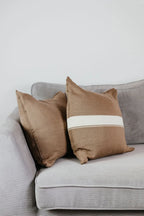 Zwei Strick-Dekokissen in Beige einfarbig und Beige mit cremefarbenem Streifen auf hellgrauem Sofa im Wohnbeispiel.