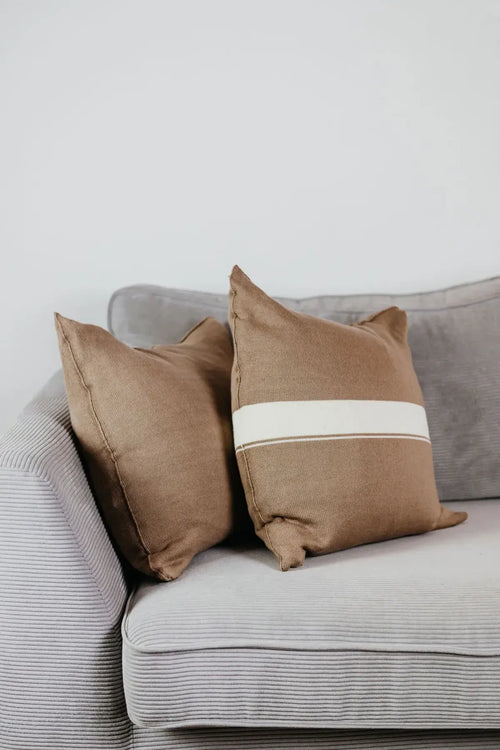 Zwei Strick-Dekokissen in Beige einfarbig und Beige mit cremefarbenem Streifen auf hellgrauem Sofa im Wohnbeispiel.