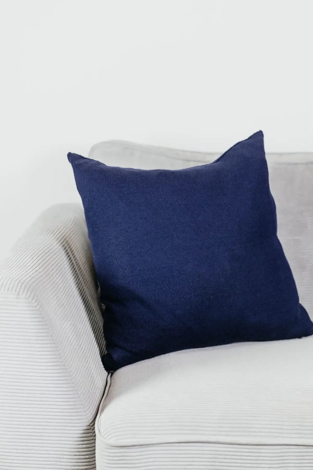 Navyblaues Strick-Dekokissen auf einem hellgrauen Sofa vor einer weißen Wand.