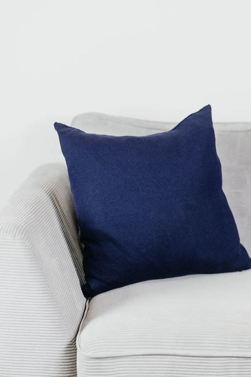 Navyblaues Strick-Dekokissen auf einem hellgrauen Sofa vor einer weißen Wand.