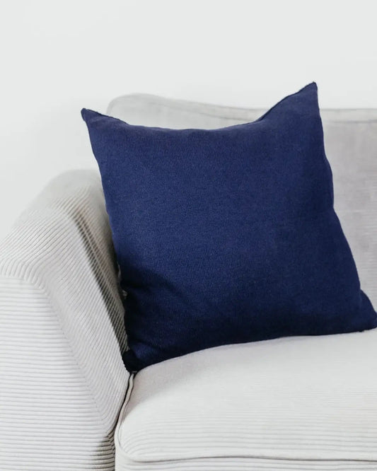 Navyblaues Strick-Dekokissen auf einem hellgrauen Sofa vor einer weißen Wand.