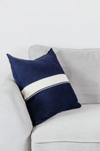 Navyblaues Strick-Dekokissen mit cremefarbenem Streifen auf einem hellgrauen Sofa vor einer weißen Wand.