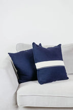 Zwei Strick-Dekokissen in Navyblau einfarbig und Navyblau mit cremefarbenem Streifen auf hellgrauem Sofa im Wohnbeispiel.