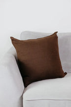 Braunes Strick-Dekokissen auf einem hellgrauen Sofa vor einer weißen Wand.