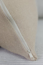 Detailaufnahme eines cremebeigen Strick-Dekokissens mit eingenähtem Reißverschluss auf einem hellen Sofa.