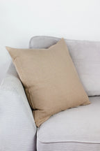 Cremebeiges Strick-Dekokissen auf einem hellgrauen Sofa vor einer weißen Wand.