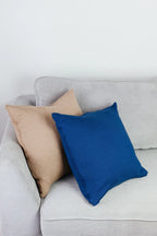 Zwei Strick-Dekokissen in den Farben Cremebeige und Indigoblau dekorativ auf einem hellgrauen Sofa im Wohnbeispiel.