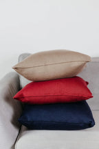 Drei Strick-Dekokissen in Cremebeige, Weinrot und Navyblau auf einem Sofa gestapelt.