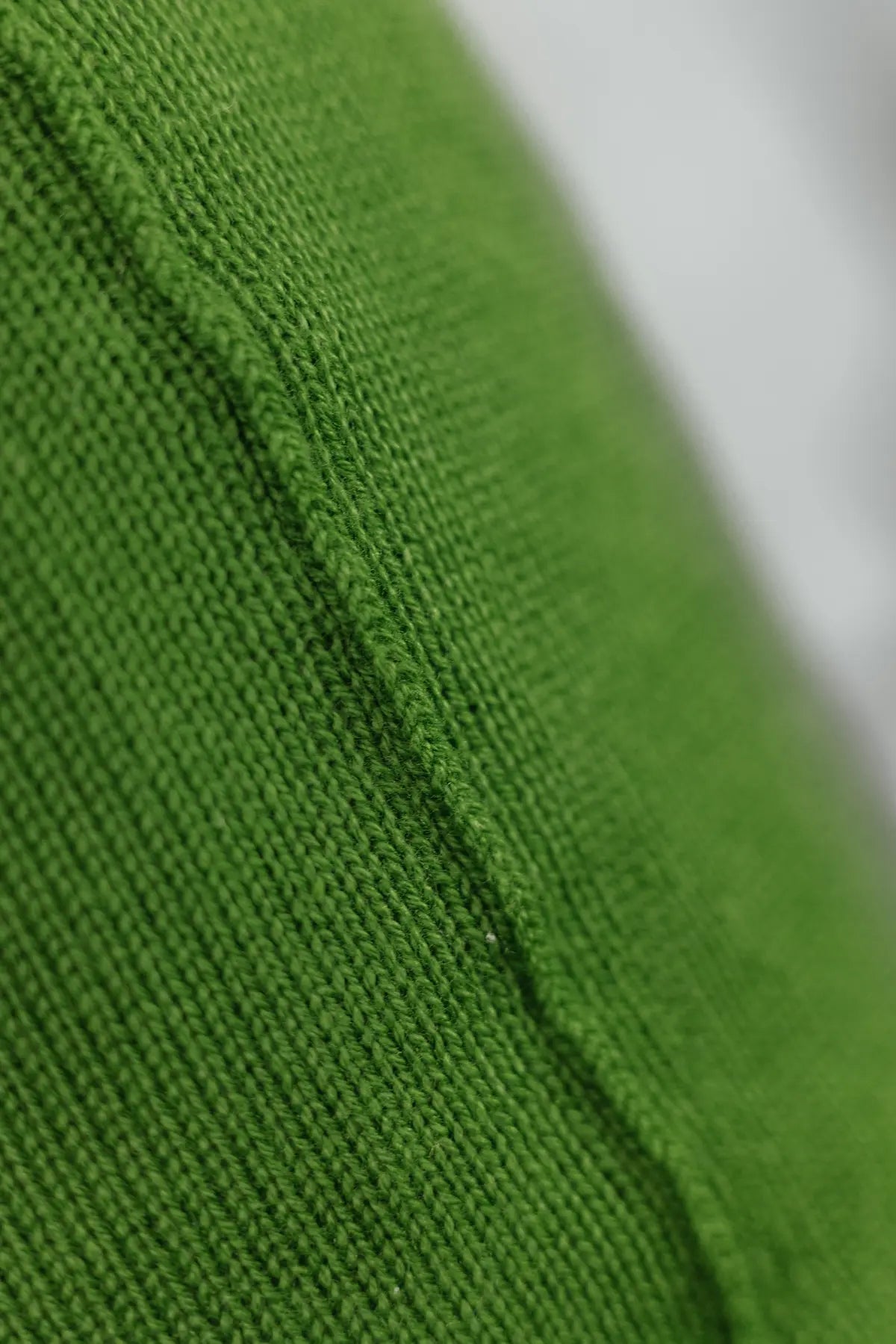 Detailaufnahme der Naht eines Strick-Dekokissens in der Farbe Grün mit sichtbarer Struktur des Strickmaterials.