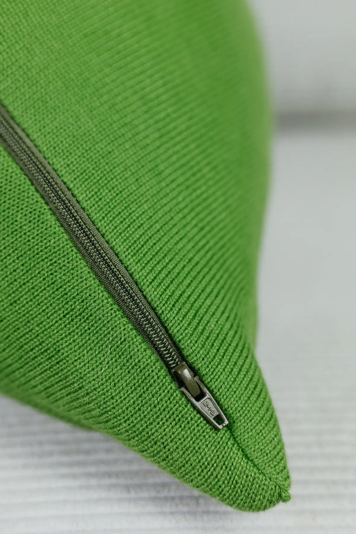 Detailaufnahme eines grünen Strick-Dekokissens mit eingenähtem Reißverschluss auf einem hellen Sofa.