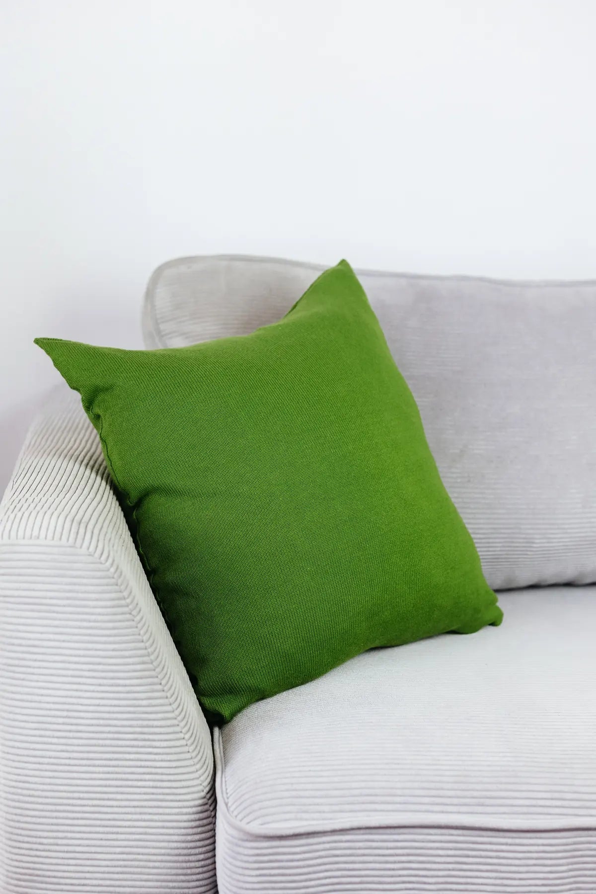 Grünes Strick-Dekokissen auf einem hellgrauen Sofa vor einer weißen Wand.