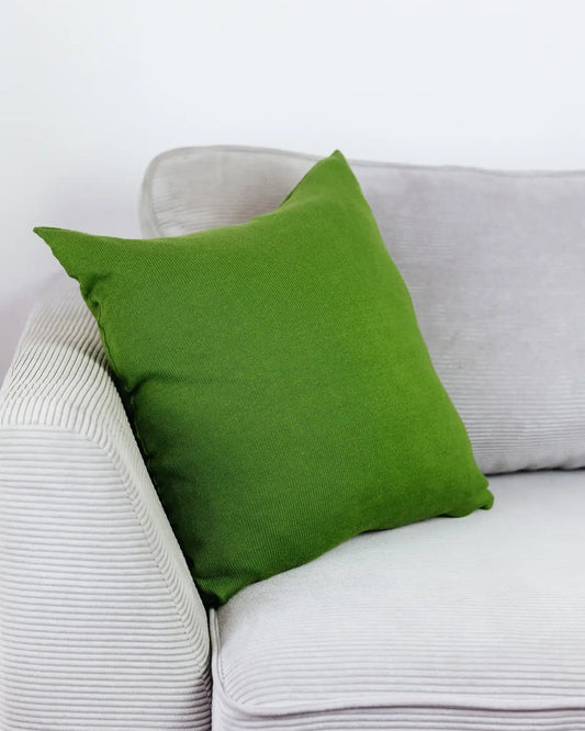 Grünes Strick-Dekokissen auf einem hellgrauen Sofa vor einer weißen Wand.