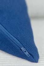 Detailaufnahme eines indigoblauen Strick-Dekokissens mit eingenähtem Reißverschluss auf einem hellen Sofa.