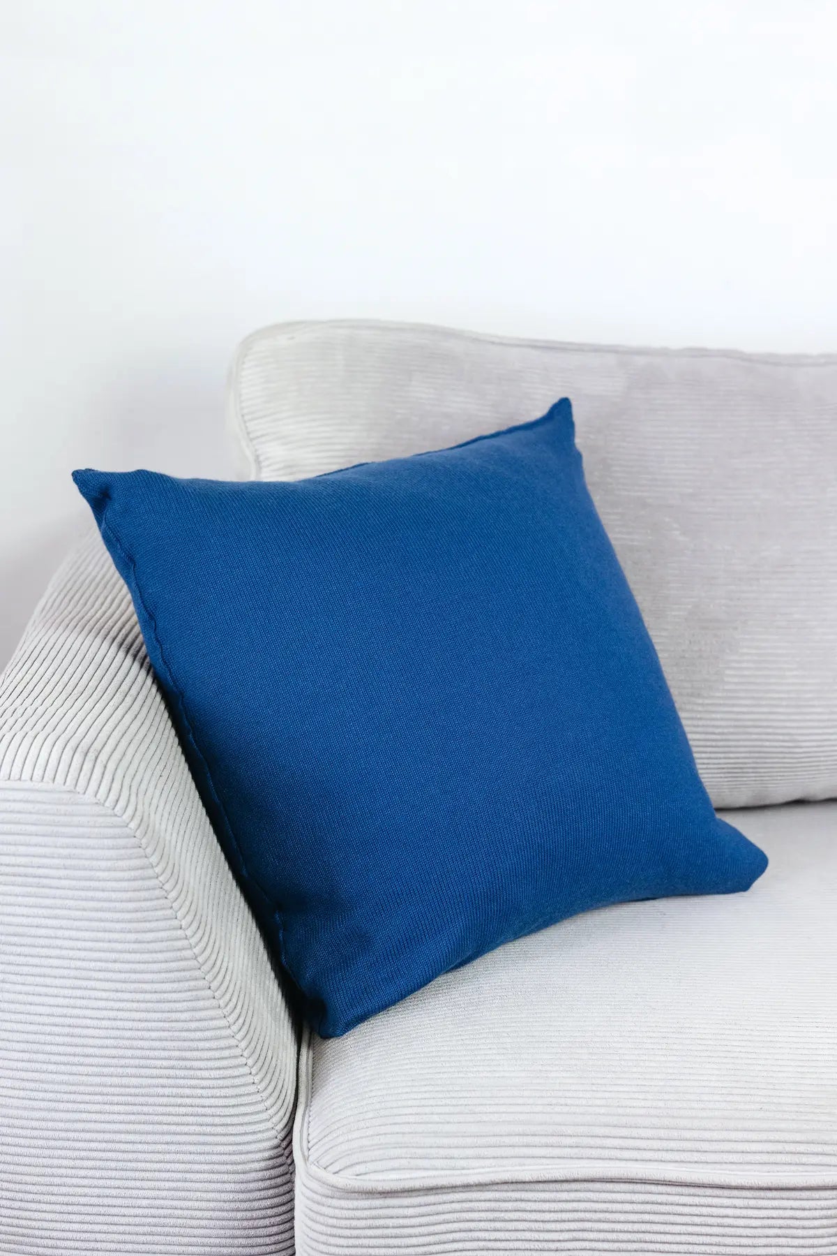 Indigoblaues Strick-Dekokissen auf einem hellgrauen Sofa vor einer weißen Wand.