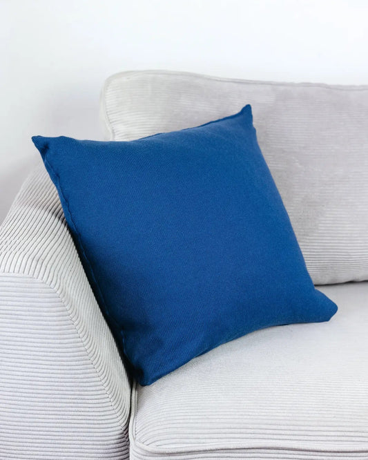Indigoblaues Strick-Dekokissen auf einem hellgrauen Sofa vor einer weißen Wand.