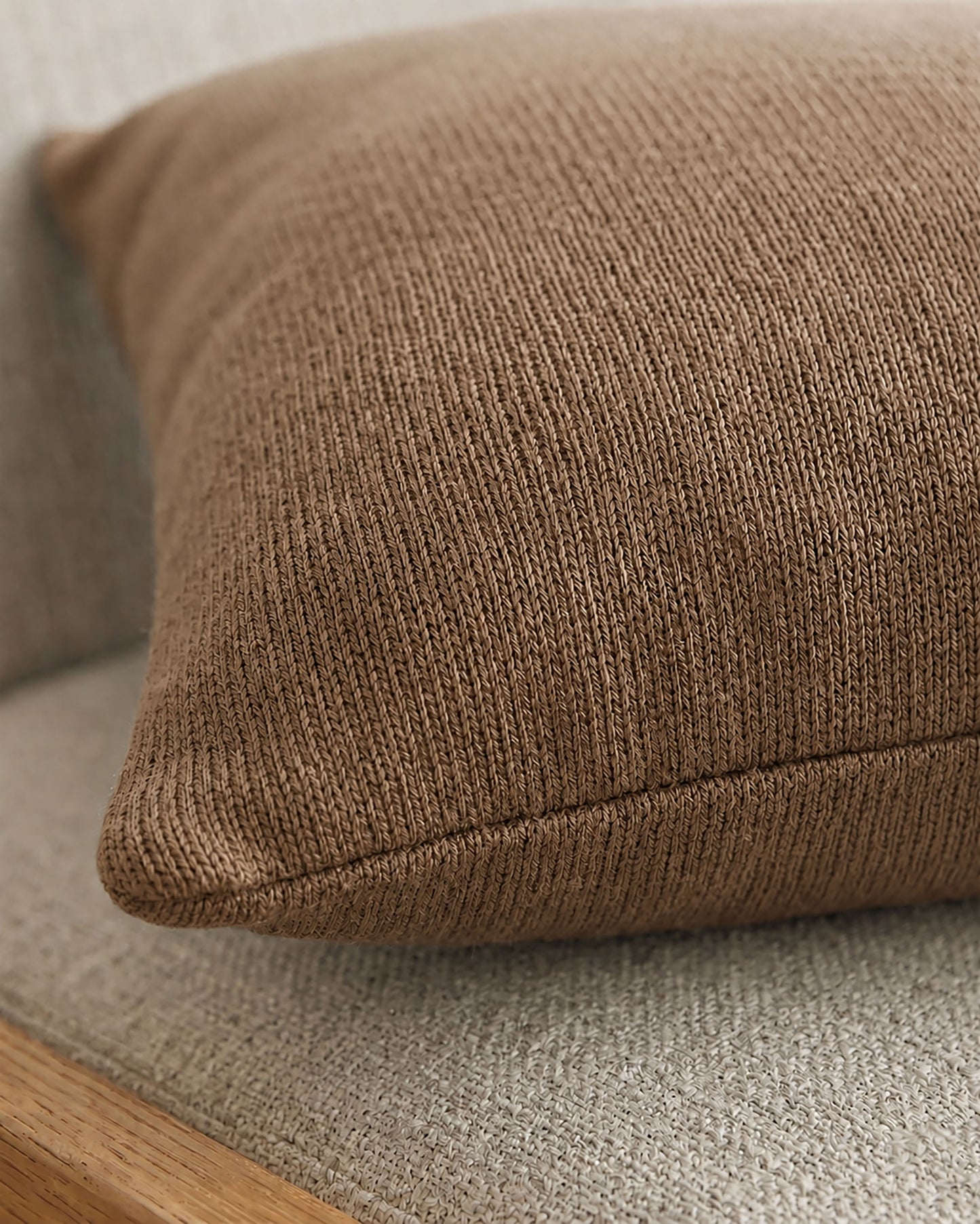 Detailaufnahme eines Dekokissens in Beige mit feiner Struktur und sauber verarbeiteter Naht auf beigem Polstersessel.