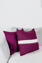 Zwei Strick-Dekokissen in Beerenfarben einfarbig und Beerenfarben mit cremefarbenem Streifen auf hellgrauem Sofa im Wohnbeispiel.