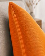 Detailaufnahme eines orangenen Dekokissens mit sichtbarem Reißverschluss auf einem beigen Sessel.
