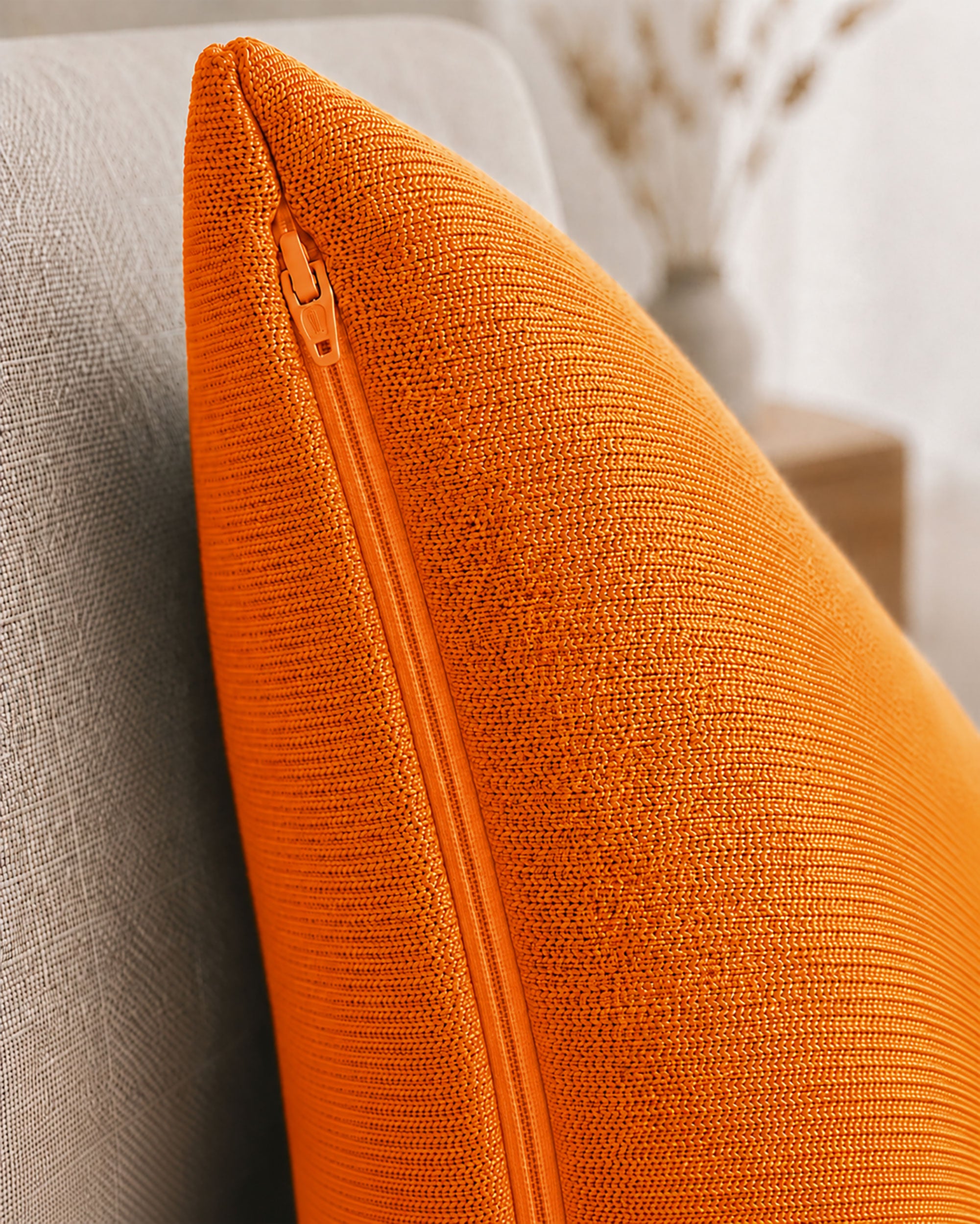 Detailaufnahme eines orangenen Dekokissens mit sichtbarem Reißverschluss auf einem beigen Sessel.