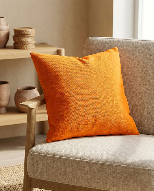 Orangens Dekokissen auf einem beigen Sofa in einem warm eingerichteten Wohnzimmer mit Holzregal und Zimmerpflanze im Hintergrund.