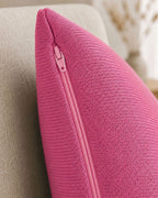Detailaufnahme eines pinken Dekokissens mit sichtbarem Reißverschluss auf einem beigen Sessel.