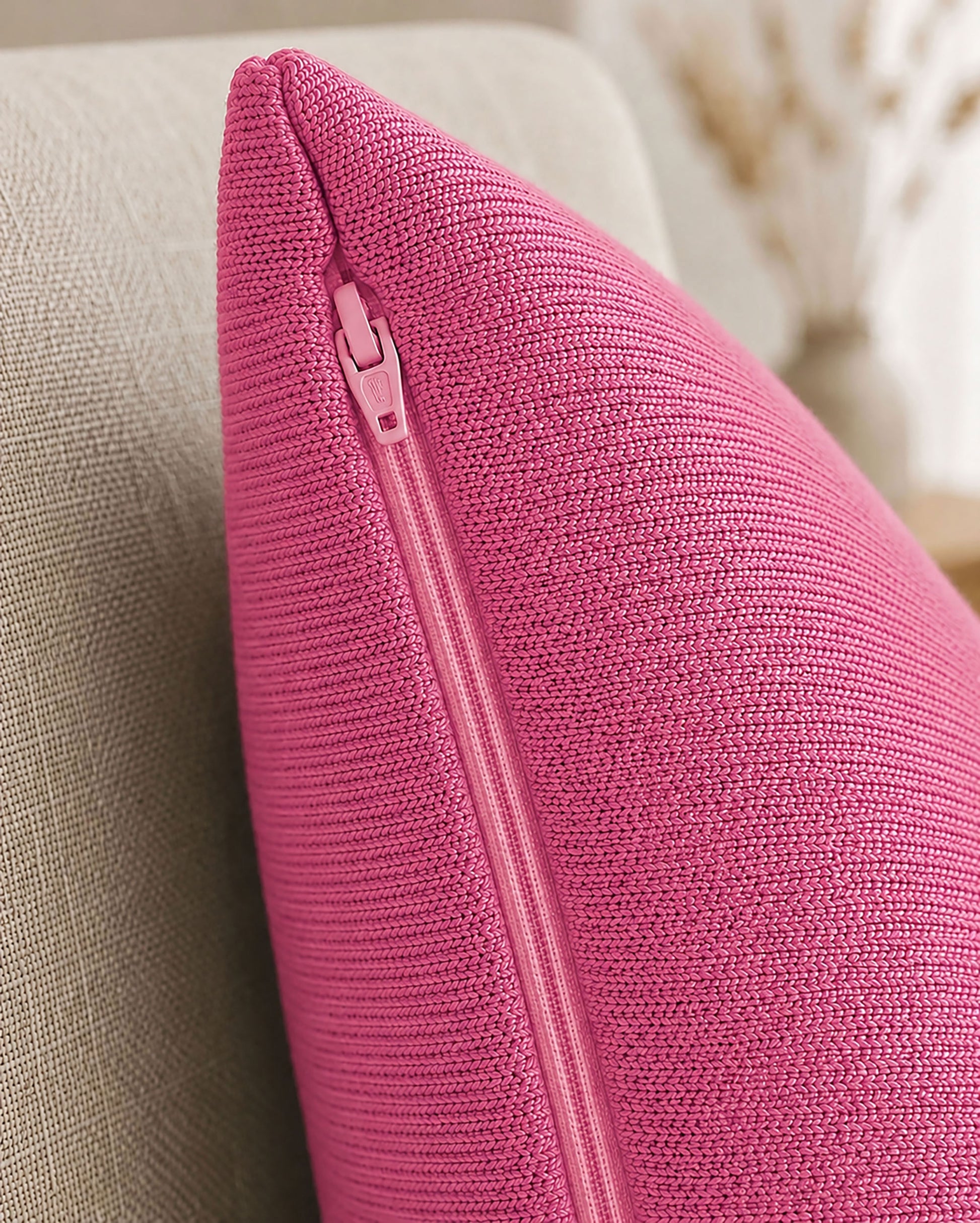 Detailaufnahme eines pinken Dekokissens mit sichtbarem Reißverschluss auf einem beigen Sessel.