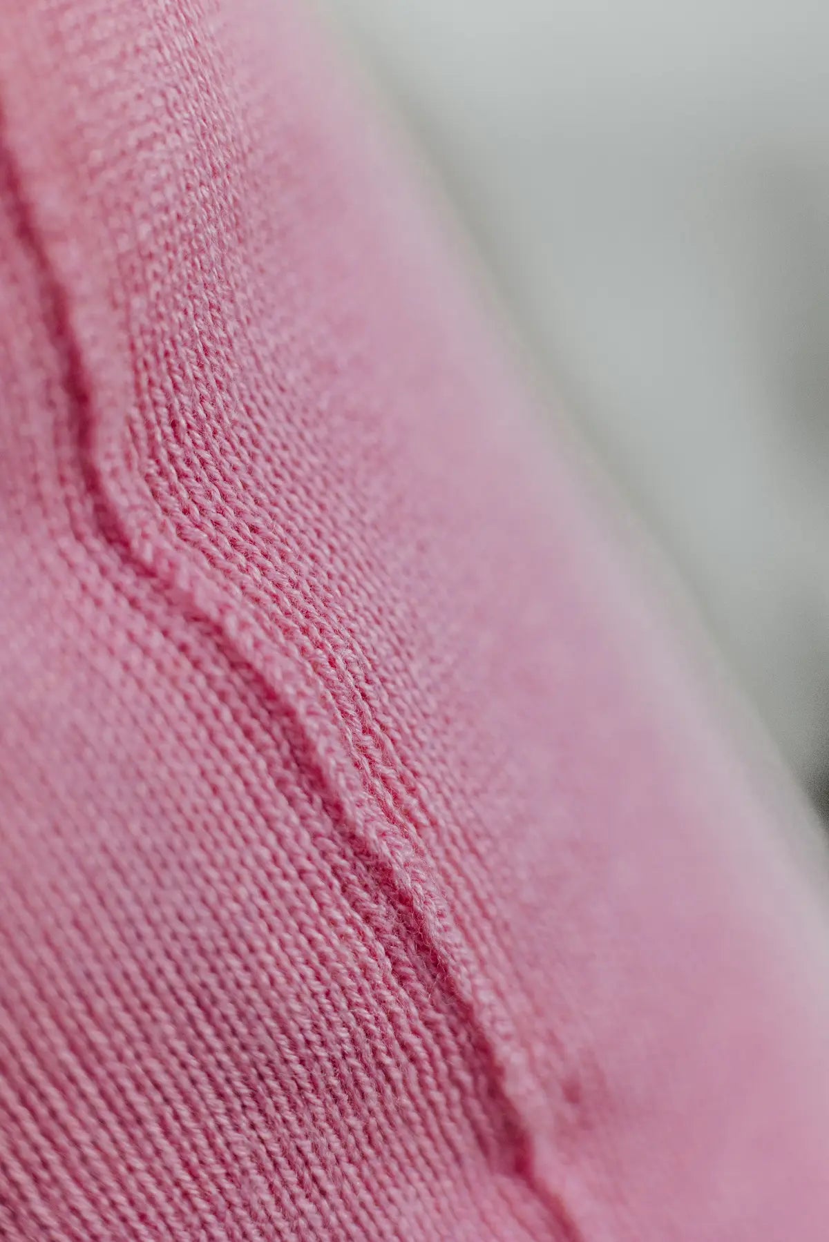 Detailaufnahme der Naht eines Strick-Dekokissens in der Farbe Rosa mit sichtbarer Struktur des Strickmaterials.