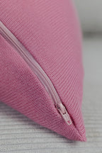 Detailaufnahme eines rosa Strick-Dekokissens mit eingenähtem Reißverschluss auf einem hellen Sofa.