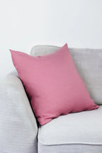 Rosa Strick-Dekokissen auf einem hellgrauen Sofa vor einer weißen Wand.