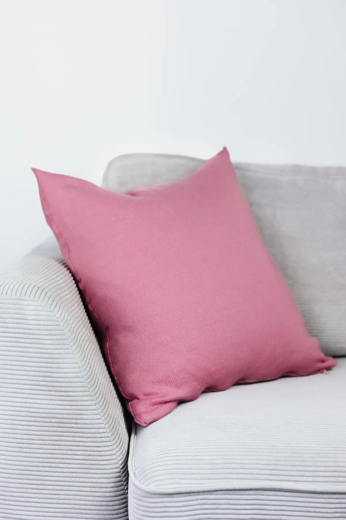 Rosa Strick-Dekokissen auf einem hellgrauen Sofa vor einer weißen Wand.