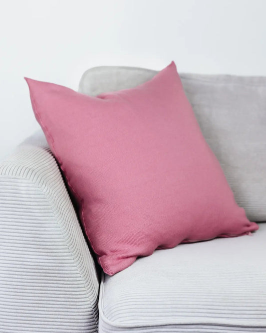 Rosa Strick-Dekokissen auf einem hellgrauen Sofa vor einer weißen Wand.