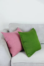 Zwei Strick-Dekokissen in den Farben Rosa und Grün dekorativ auf einem hellgrauen Sofa im Wohnbeispiel.