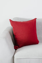 Weinrotes Strick-Dekokissen auf einem hellgrauen Sofa vor einer weißen Wand.