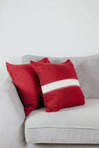 Zwei Strick-Dekokissen in Weinrot einfarbig und Weinrot mit cremefarbenem Streifen auf hellgrauem Sofa im Wohnbeispiel.