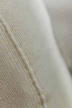 Detailaufnahme der Naht eines Strick-Dekokissens in der Farbe Cremeweiß mit sichtbarer Struktur des Strickmaterials.