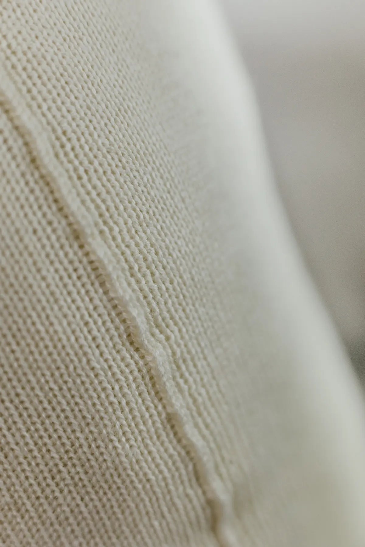 Detailaufnahme der Naht eines Strick-Dekokissens in der Farbe Cremeweiß mit sichtbarer Struktur des Strickmaterials.