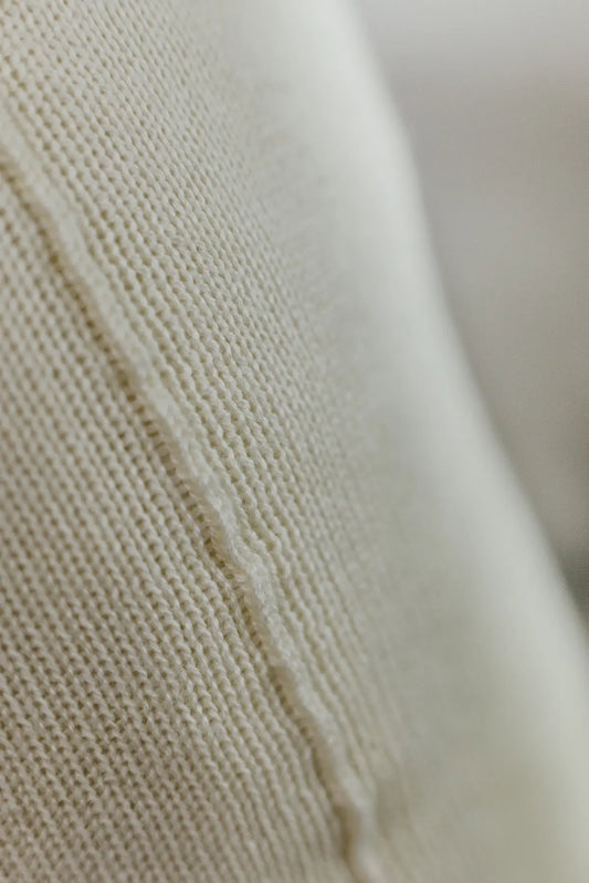Detailaufnahme der Naht eines Strick-Dekokissens in der Farbe Cremeweiß mit sichtbarer Struktur des Strickmaterials.