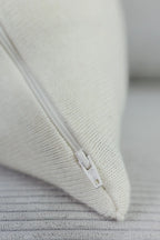 Detailaufnahme eines cremeweißen Strick-Dekokissens mit eingenähtem Reißverschluss auf einem hellen Sofa.
