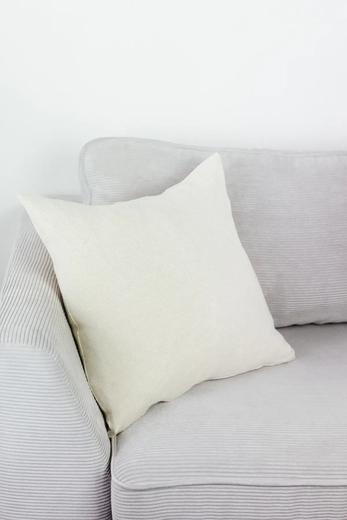 Cremeweißes Strick-Dekokissen auf einem hellgrauen Sofa vor einer weißen Wand.