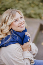 Frau kombiniert Strickschal in Navyblau-Melange mit beigen Mantel auf Treppe sitzend.