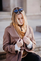 Frau trägt Strickschal in Curry-Melange im Lifestyle-Bild auf Stufen sitzend.