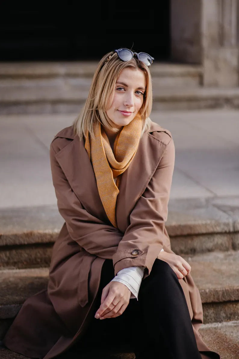 Outfit mit Strickschal in Curry-Melange getragen von Frau in braunem Mantel im herbstlichen Look.